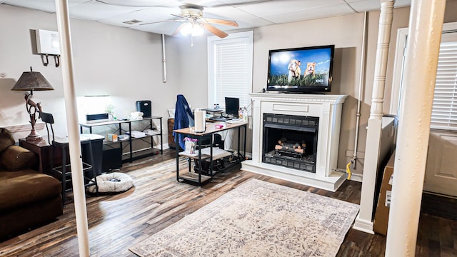 living room with baseboards, a fireplace with raised hearth, a ceiling fan, wood finished floors, and a paneled ceiling