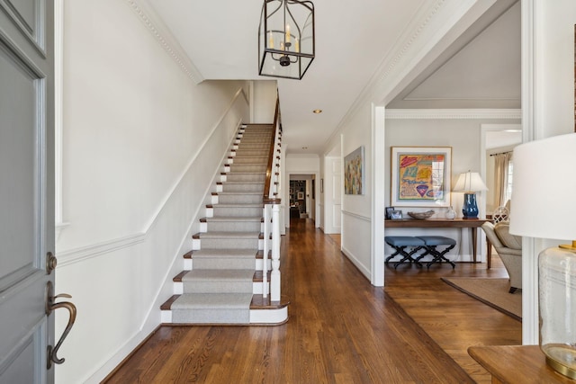 entryway with an inviting chandelier, crown molding, stairway, and dark wood-type flooring