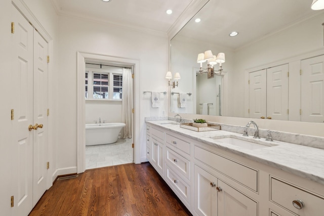 bathroom featuring a freestanding tub, wood finished floors, a sink, double vanity, and crown molding