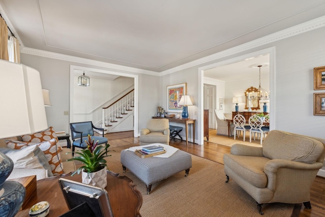 living area featuring ornamental molding, stairway, wood finished floors, and a notable chandelier