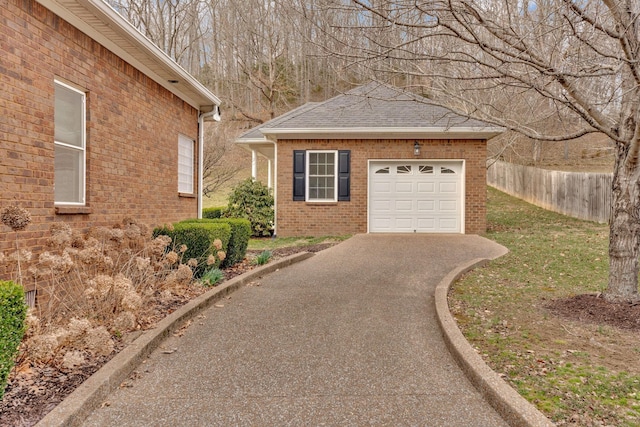 view of side of property with aphalt driveway, an attached garage, brick siding, fence, and roof with shingles