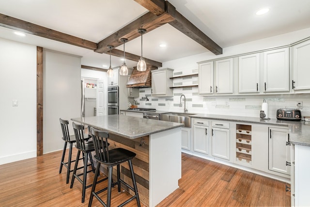 kitchen featuring dark stone counters, light wood-style flooring, hanging light fixtures, double oven, and open shelves