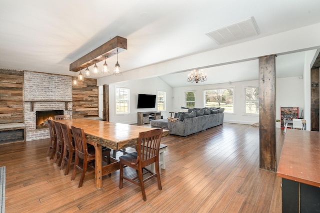 dining room featuring visible vents, wood finished floors, vaulted ceiling with beams, a fireplace, and a notable chandelier