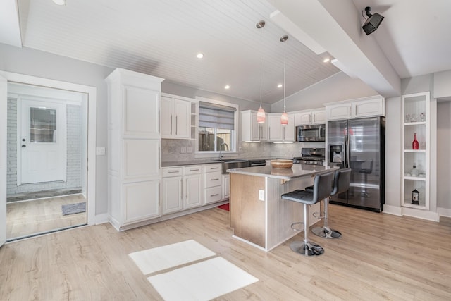 kitchen with stainless steel appliances, a sink, white cabinets, hanging light fixtures, and a center island