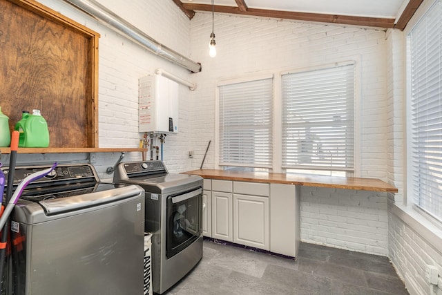 laundry area featuring tankless water heater, cabinet space, brick wall, and separate washer and dryer