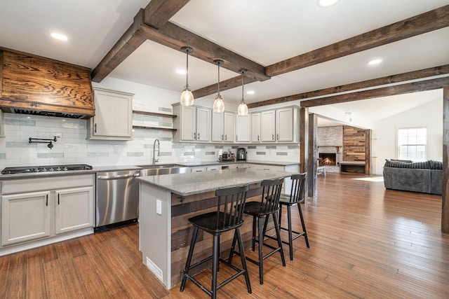 kitchen featuring light stone counters, stainless steel appliances, a sink, a kitchen island, and decorative light fixtures