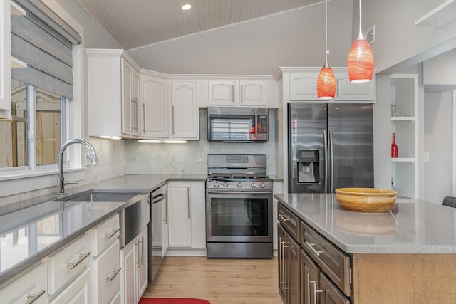 kitchen with pendant lighting, lofted ceiling, appliances with stainless steel finishes, white cabinetry, and a kitchen island