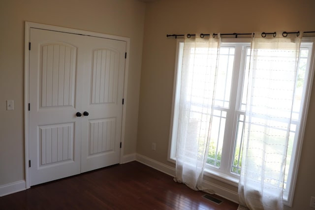 unfurnished bedroom with dark wood-style floors, a closet, visible vents, and baseboards