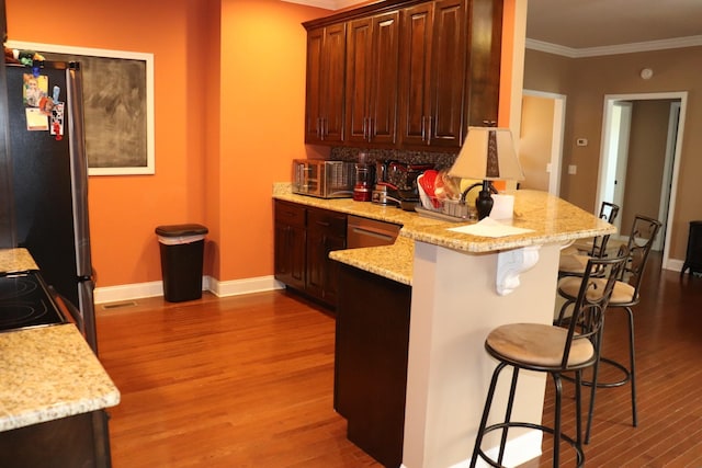 kitchen with a breakfast bar, crown molding, light wood finished floors, freestanding refrigerator, and a peninsula