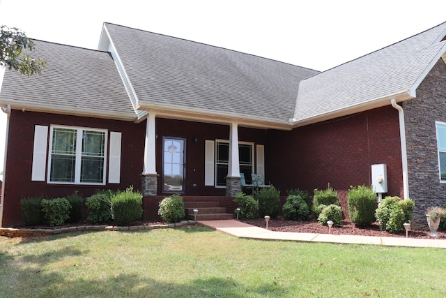 view of front of home with brick siding, a shingled roof, covered porch, and a front yard