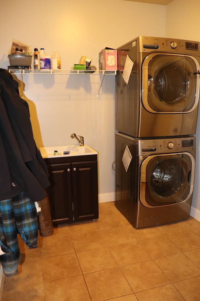 clothes washing area featuring light tile patterned floors, stacked washer / dryer, a sink, baseboards, and cabinet space