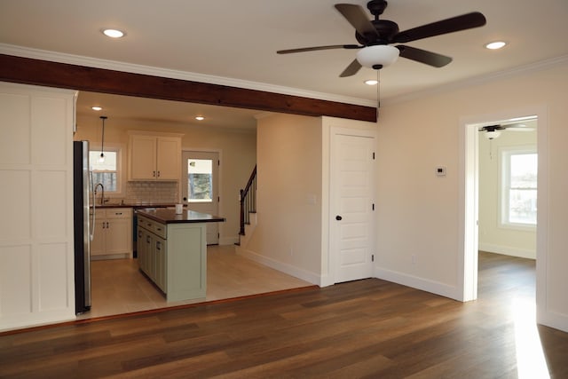 kitchen with dark wood finished floors, dark countertops, a kitchen island, freestanding refrigerator, and crown molding