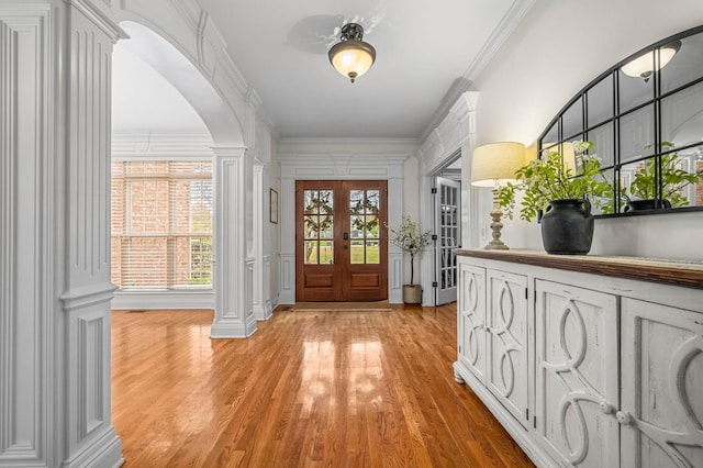 entryway featuring arched walkways, french doors, ornamental molding, light wood-type flooring, and ornate columns