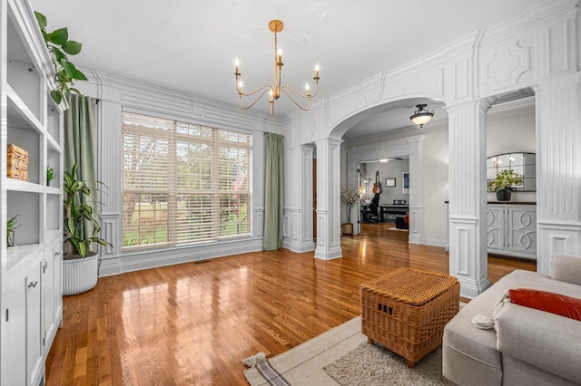 living area with arched walkways, a notable chandelier, a decorative wall, and decorative columns