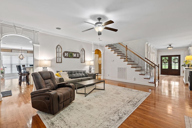 living area with visible vents, arched walkways, a ceiling fan, light wood-style flooring, and stairway