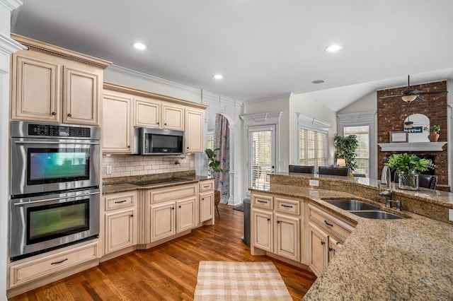 kitchen featuring light stone counters, light wood finished floors, stainless steel appliances, backsplash, and a sink