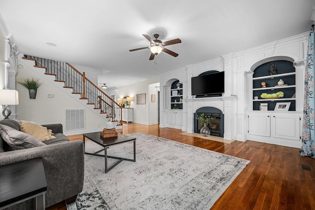 living area with built in features, dark wood-style flooring, visible vents, a fireplace with flush hearth, and stairs