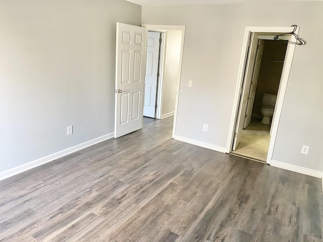 unfurnished bedroom with dark wood-style flooring, ensuite bath, and baseboards