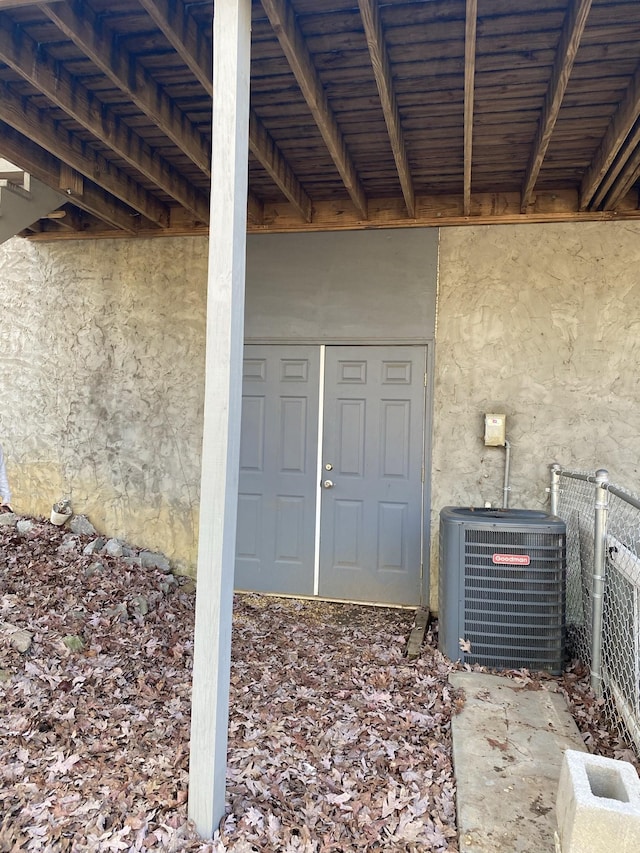 doorway to property featuring fence, central AC unit, and stucco siding