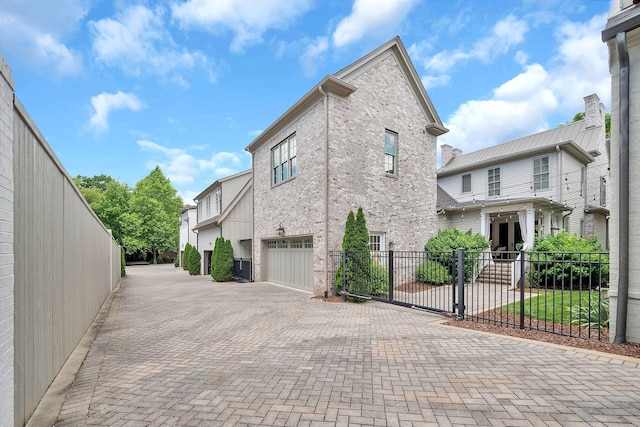 view of home's exterior featuring a garage, brick siding, decorative driveway, and fence