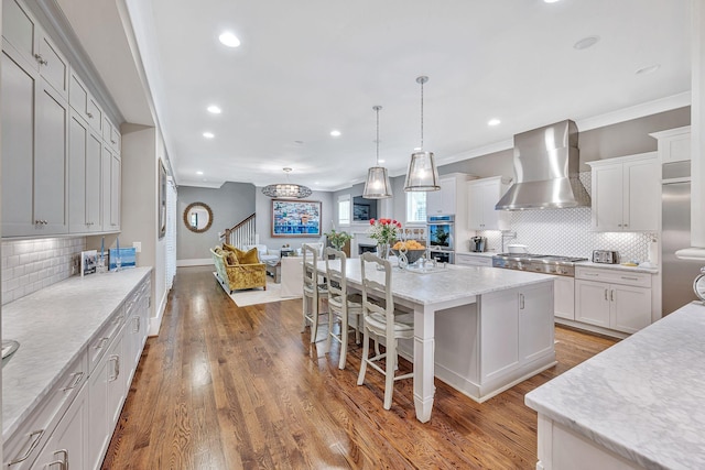 kitchen with white cabinets, wall chimney exhaust hood, open floor plan, a center island, and pendant lighting