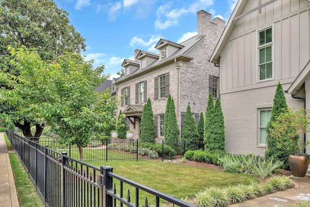 exterior space featuring brick siding, fence, a lawn, board and batten siding, and a chimney