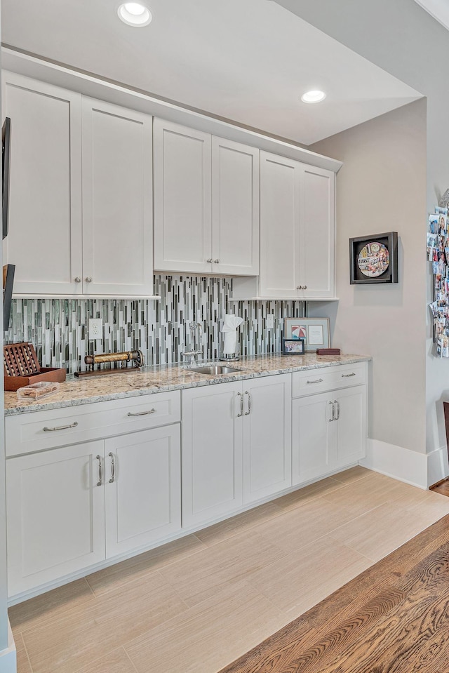 kitchen featuring tasteful backsplash, recessed lighting, white cabinetry, a sink, and light stone countertops