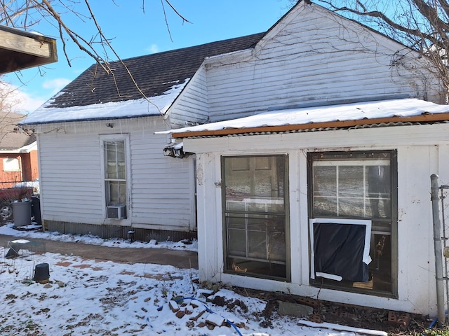 snow covered rear of property featuring a shingled roof and cooling unit