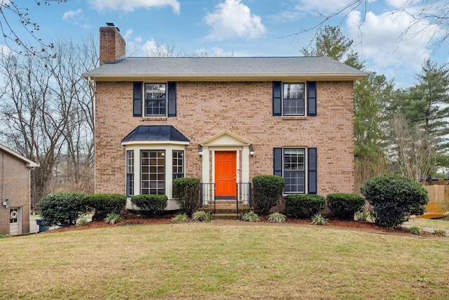 colonial house with brick siding, a chimney, and a front yard