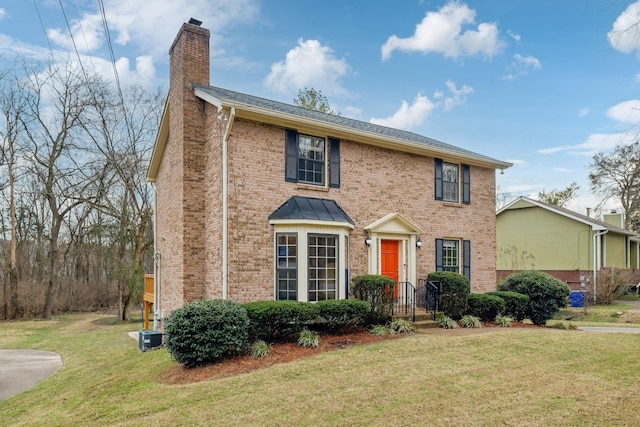 colonial inspired home featuring brick siding, a chimney, and a front yard