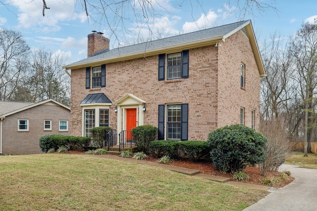 colonial home with brick siding, a chimney, and a front lawn