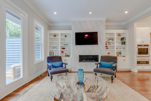 sitting room featuring light wood-style floors, a wealth of natural light, a large fireplace, and ornamental molding