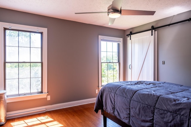 bedroom featuring a barn door, baseboards, a ceiling fan, wood finished floors, and a textured ceiling