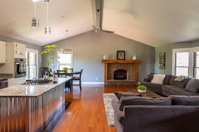 living area featuring light wood-style floors, a fireplace, lofted ceiling with beams, and baseboards