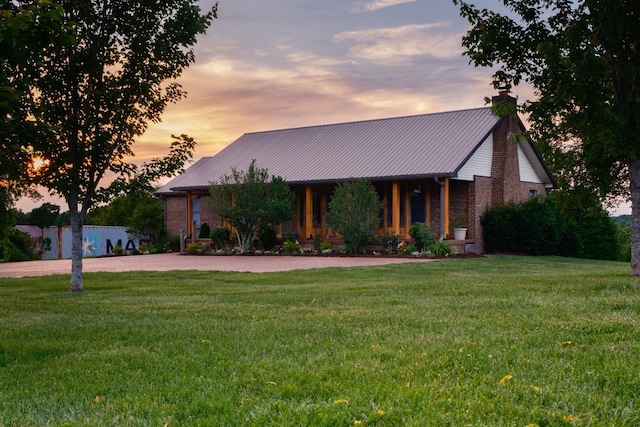 view of front of property featuring metal roof, a front lawn, a chimney, and brick siding