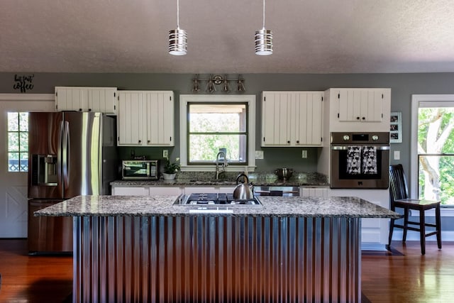 kitchen with white cabinets, appliances with stainless steel finishes, light stone counters, hanging light fixtures, and a sink