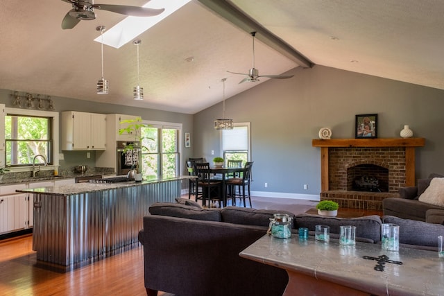 kitchen featuring vaulted ceiling with skylight, white cabinets, wood finished floors, a brick fireplace, and a sink