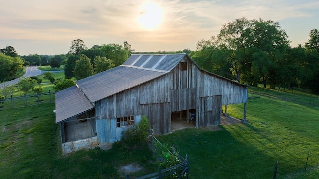 outdoor structure at dusk with a barn, fence, an outdoor structure, and a yard