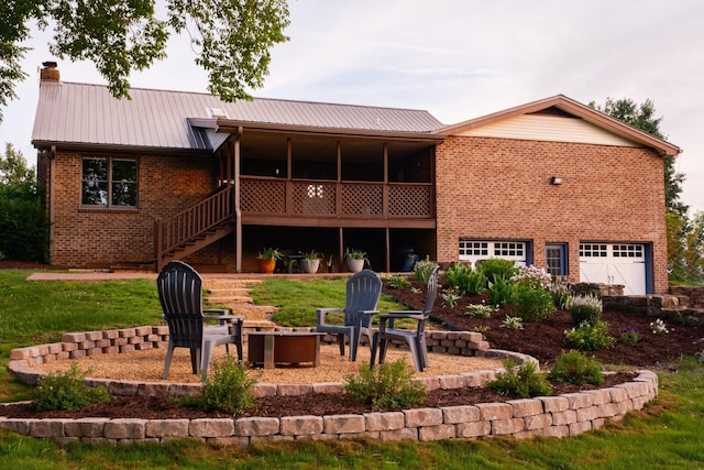 back of house featuring brick siding, a chimney, metal roof, a garage, and a fire pit