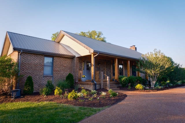 view of front of house featuring covered porch, metal roof, brick siding, and a chimney