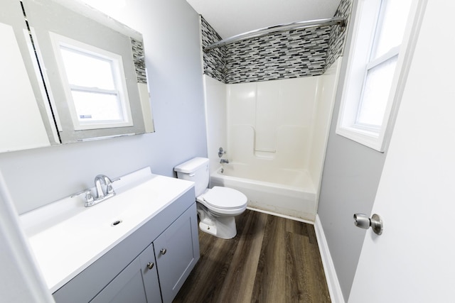 bathroom with toilet, wood finished floors, vanity, baseboards, and shower / washtub combination