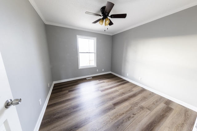 spare room featuring wood finished floors, a ceiling fan, visible vents, baseboards, and ornamental molding