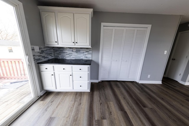 kitchen with dark countertops, decorative backsplash, dark wood-type flooring, white cabinets, and baseboards