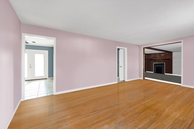 unfurnished living room with a brick fireplace, baseboards, wood finished floors, and french doors