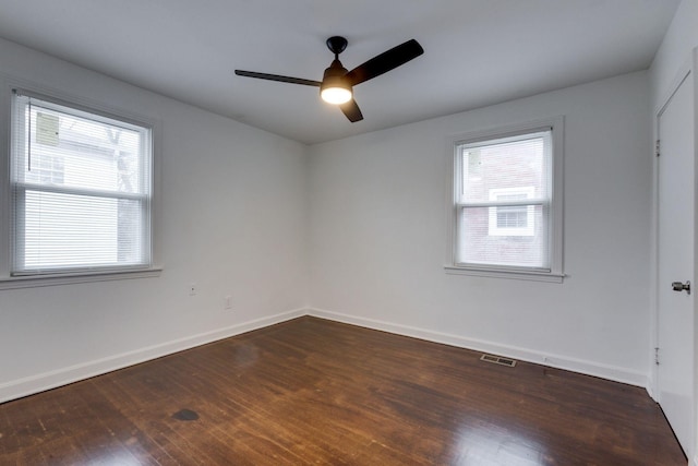 empty room with dark wood-style floors, plenty of natural light, visible vents, and baseboards