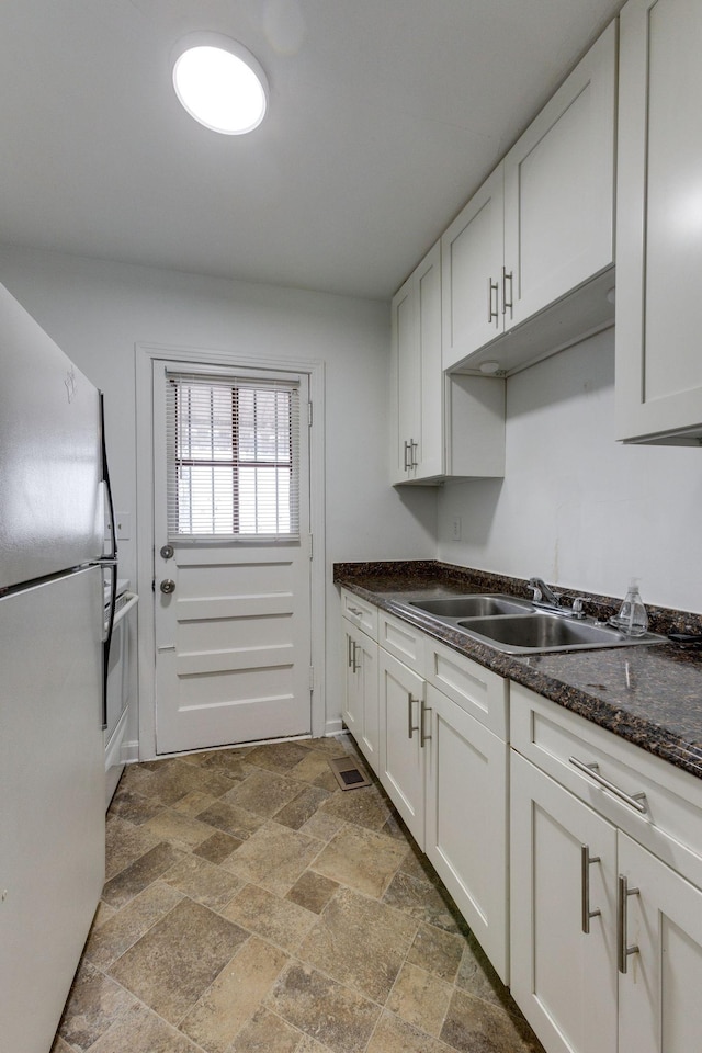 kitchen featuring stone finish floor, white cabinets, a sink, and freestanding refrigerator