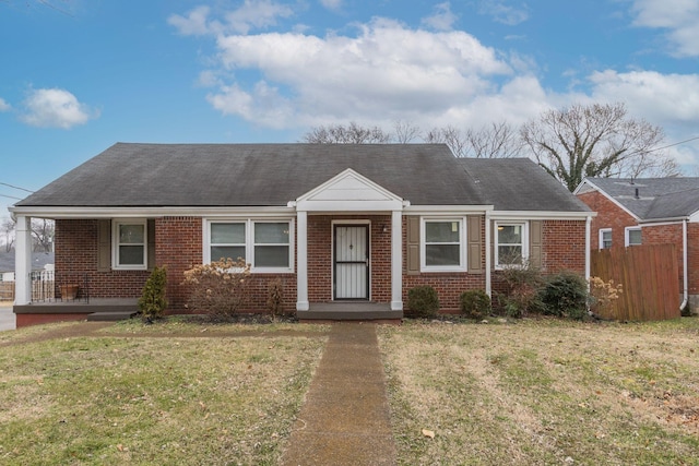 view of front of house with brick siding, roof with shingles, a front yard, and fence