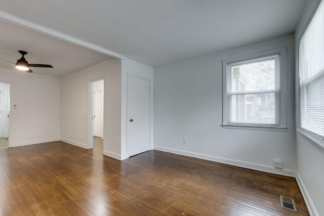 empty room featuring a ceiling fan, baseboards, visible vents, and dark wood-style flooring