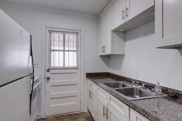 kitchen featuring dark stone counters, freestanding refrigerator, white cabinetry, and a sink