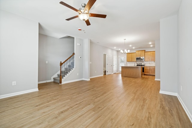 unfurnished living room with light wood-style floors, ceiling fan with notable chandelier, baseboards, and stairs